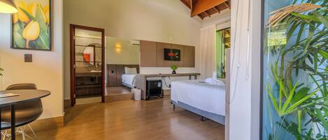 A hotel room with a bed, a desk, a TV, and a large window with plants.