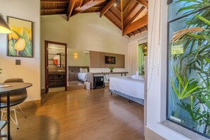 A hotel room with a bed, a desk, a TV, and a large window with plants. - Pousada Saint Diniz (Monte Sião)