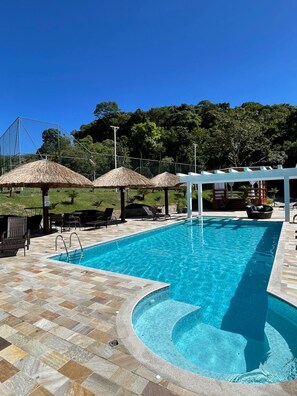 A swimming pool with a tiled deck, thatched umbrellas, and lounge chairs. - Pousada Saint Diniz (Monte Sião)