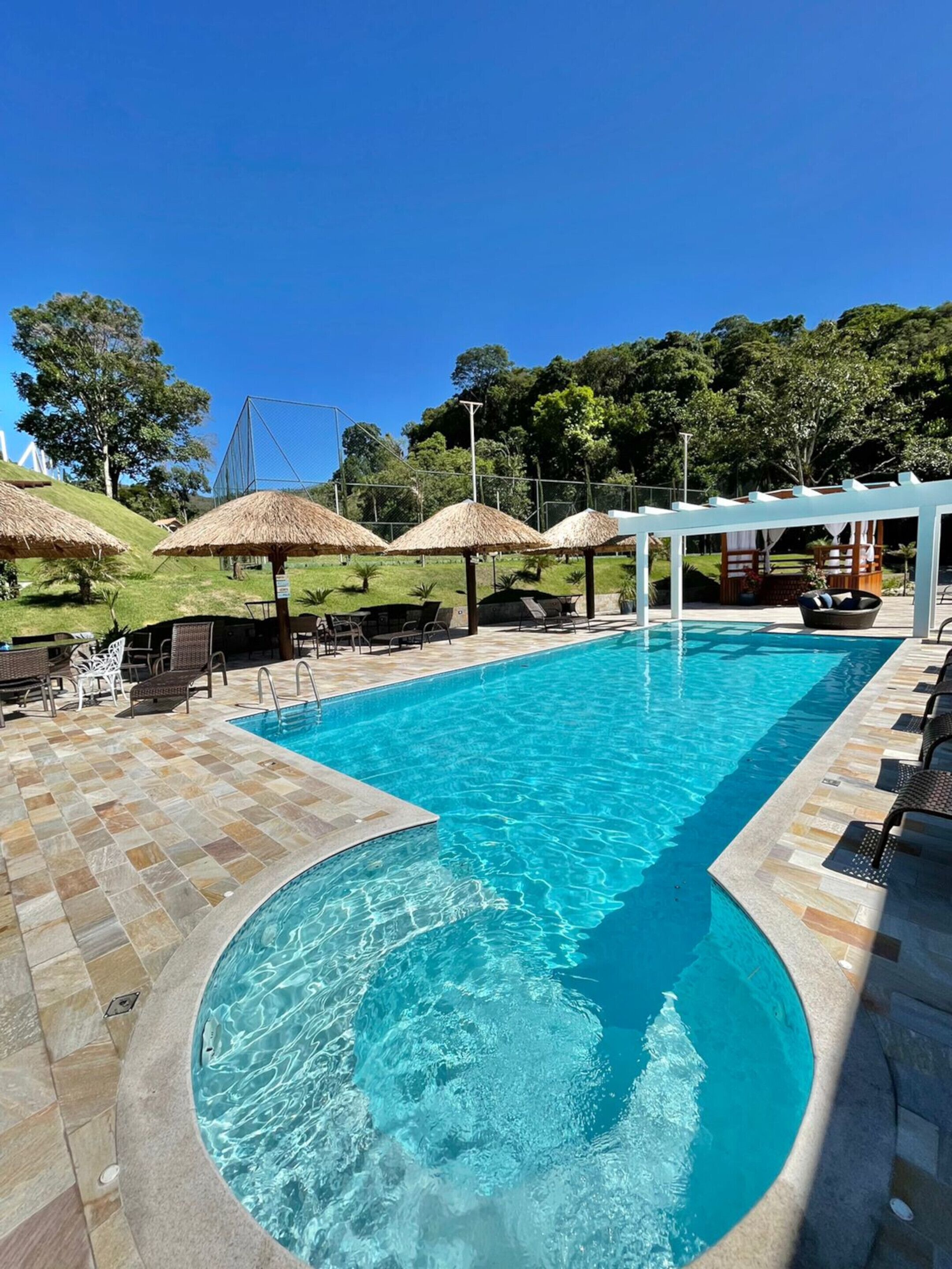 A swimming pool with a tiled deck, lounge chairs, and thatched umbrellas.