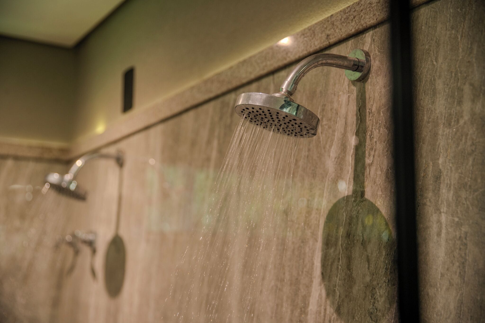 A shower area with multiple showerheads and a tiled wall.