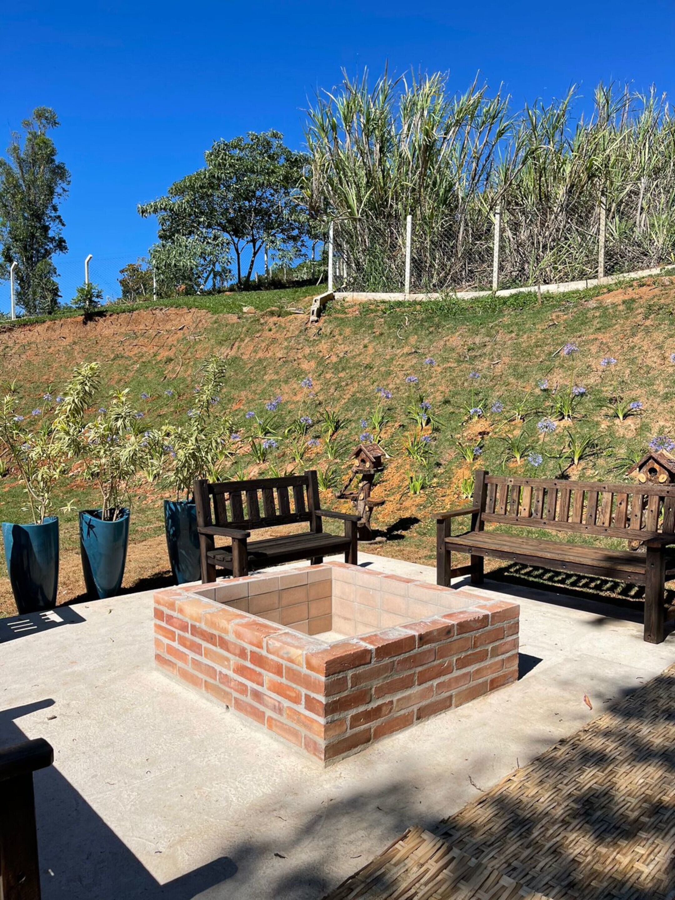 A patio area with two wooden benches, a brick fire pit, and potted plants.
