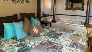 Een slaapkamer met een groot bed, een decoratief wandobject, een badkamer met bad en spiegel, en een houten stoel.