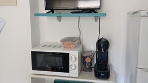 Et tekøkken med mikroovn, kaffemaskine og et fjernsyn på en hylde.