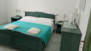 En pænt redt seng med en turkis dyne og hvide puder, et lille natbord med en lampe, og en sengebord med en lampe.