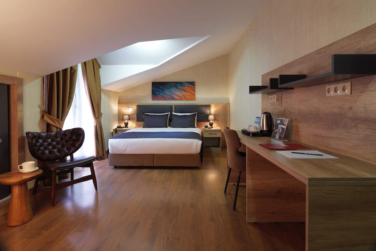 A modern hotel room with a large bed, a desk, a chair, and a small table with a cup.