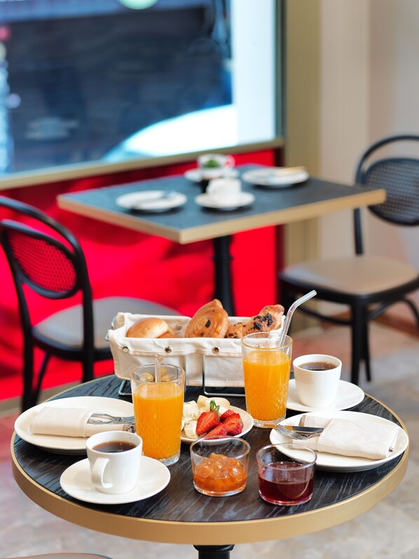 A breakfast setting with a table set for two, including plates, cups, and a basket of pastries.