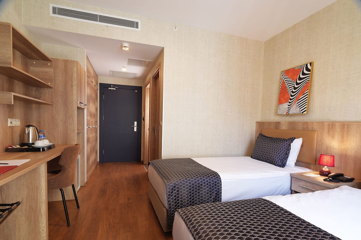 A hotel room with two beds, a desk with a coffee maker, a chair, and a painting on the wall.