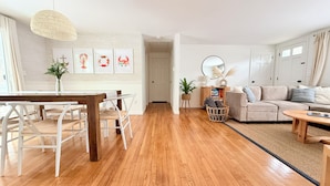 Un salon spacieux doté d’un plancher en bois, un coin repas avec une table et des chaises en bois, et un canapé beige.