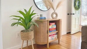 Un coin agrémenté d’un présentoir à plantes en osier, d’une petite bibliothèque remplie de livres, d’un miroir et d’une porte décorée d’une guirlande.