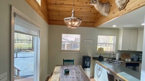 Un grand espace à manger avec une table et des chaises en bois, une cuisine avec un bar et un plafond orné de têtes de cerf.