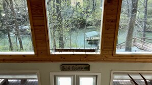 Une cabane avec vue sur une forêt et un quai surplombant une étendue d’eau.