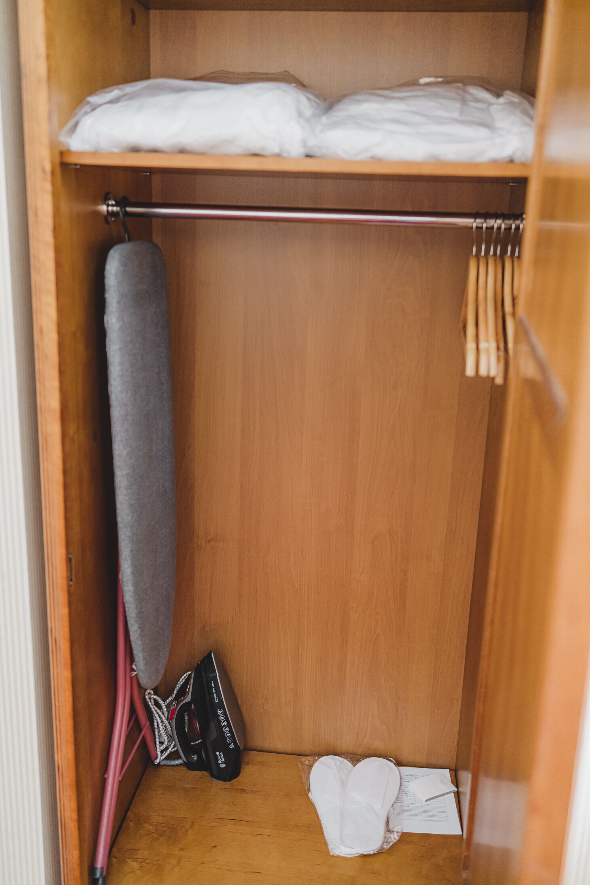 A wooden closet with a hanging rack, a pair of shoes, and a folded white shirt.