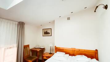 Habitación de hotel con tragaluz, una cama, un escritorio, una silla y un cuadro en la pared.