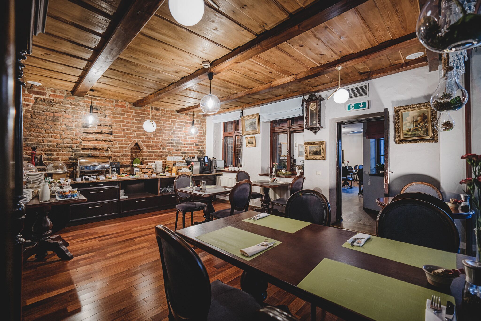 A restaurant with wooden beams, brick walls, and a brick fireplace. Tables are set with green placemats and chairs.
