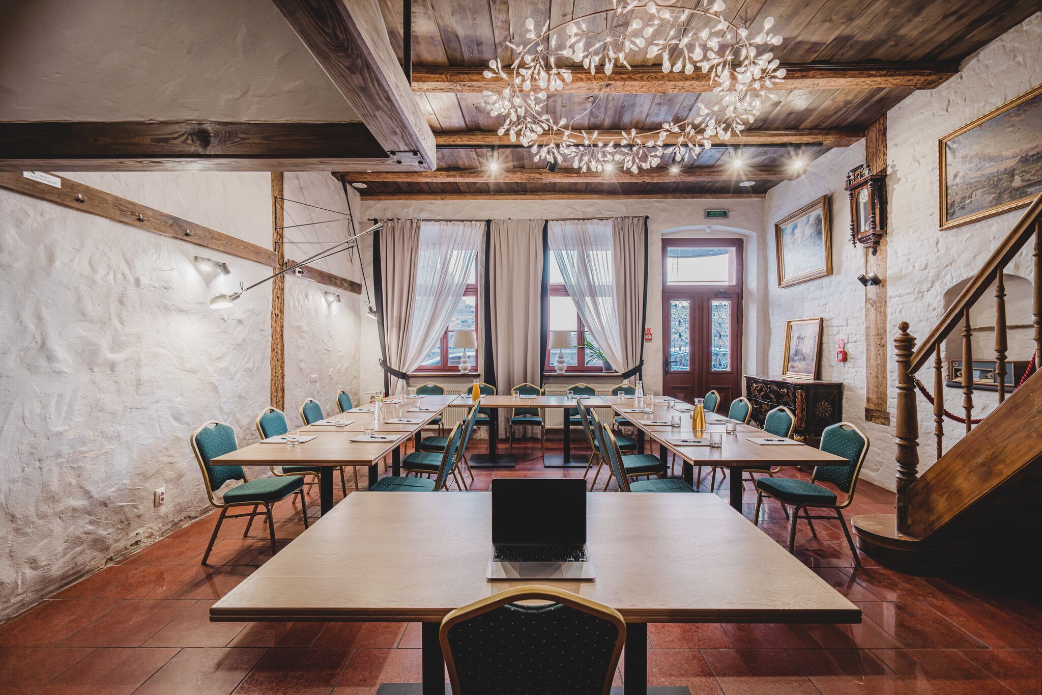 A conference room with a wooden table, chairs, a laptop, and a chandelier.