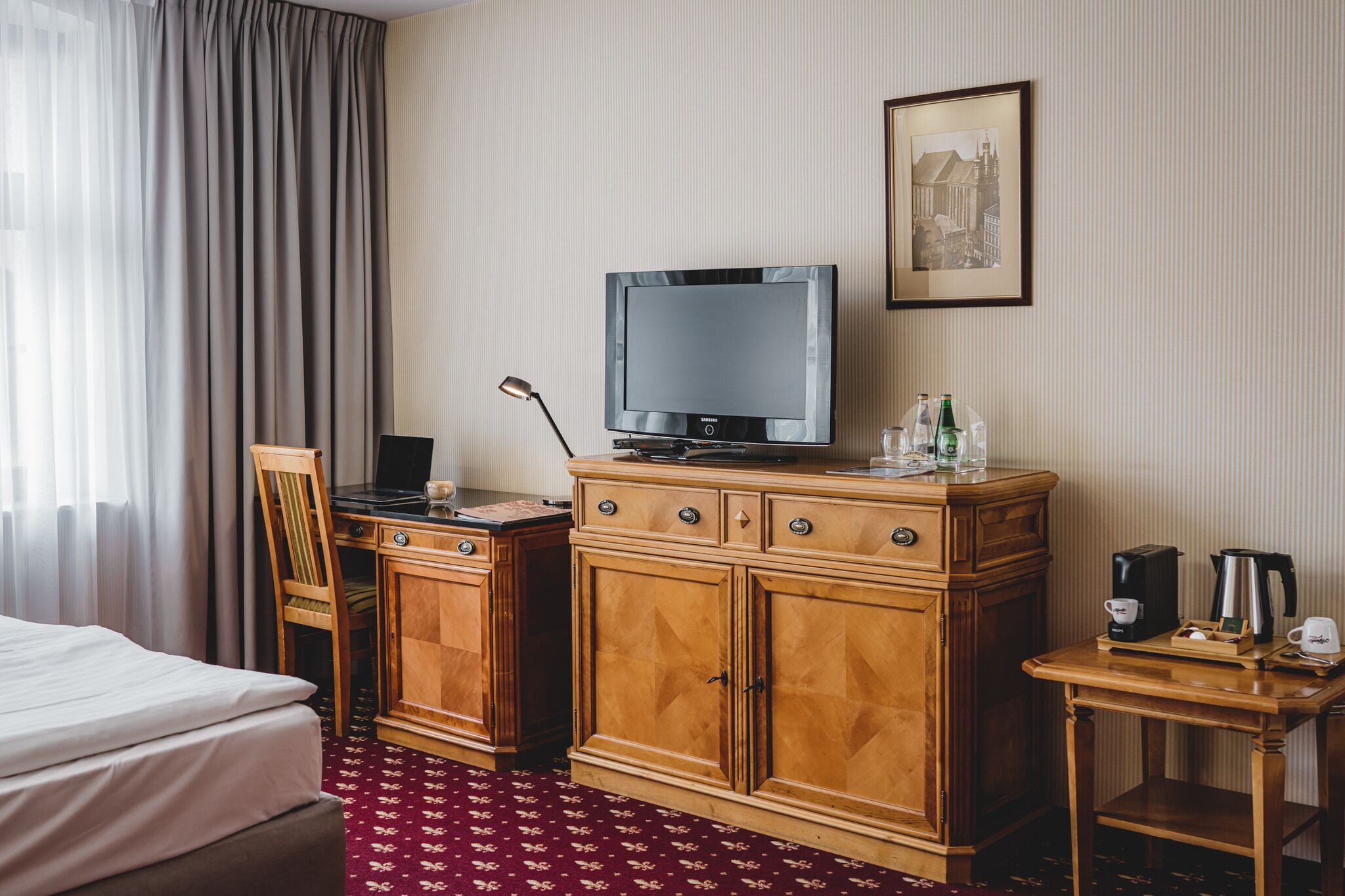 Habitación de hotel con cama, escritorio de madera, televisión y un cuadro enmarcado en la pared.