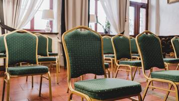 De nombreuses rangées de fauteuils verts, recouverts de tissu et dotés de cadres dorés, sont disposées dans une pièce aux grandes fenêtres et aux rideaux.