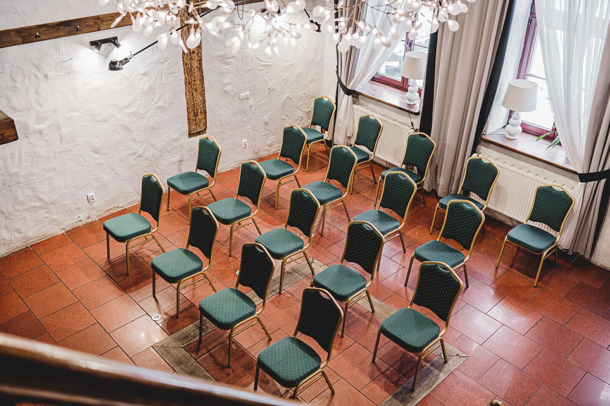 Un salón de conferencias con hileras de sillas verdes, paredes blancas y techo con vigas de madera.