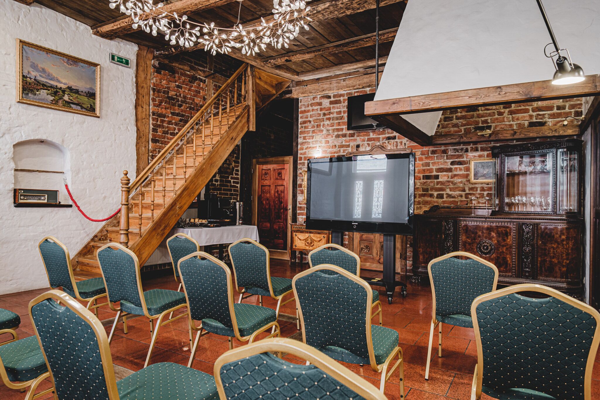A room with a brick wall, wooden staircase, a flat-screen TV, and green upholstered chairs.