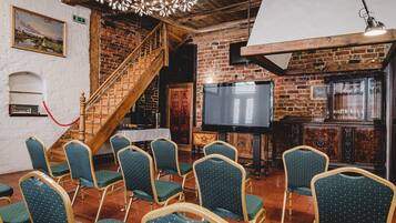 A room with a brick wall, wooden staircase, a flat-screen TV, and green upholstered chairs.