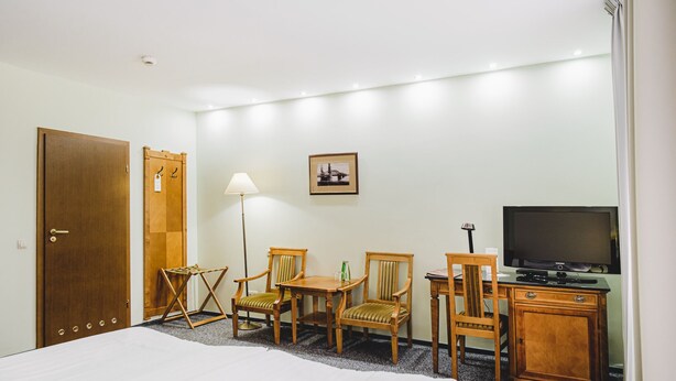 Habitación de hotel con una cama, dos sillas de madera, una mesita, televisor y un armario.