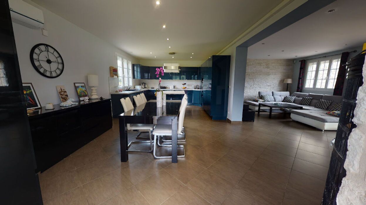 A spacious living area with a dining table, sofa, and kitchen in the background.