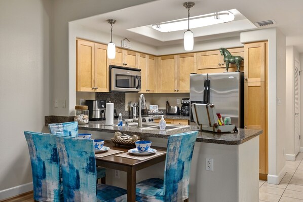A modern kitchen with wooden cabinets, stainless steel appliances, and blue chairs.