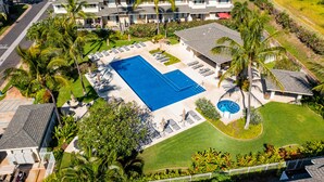 A large swimming pool surrounded by lounge chairs and palm trees, with a multi-story building in the background. - Ko'Olina Oasis: Lagoon, Pool & Resort Living (Kapolei)