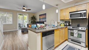 A modern kitchen with wooden cabinets, a built-in dishwasher, a microwave, and an oven. - Ko'Olina Oasis: Lagoon, Pool & Resort Living (Kapolei)
