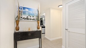 A hallway with a dark wooden console table, two vases, and a painting of a beach scene. - Ko'Olina Oasis: Lagoon, Pool & Resort Living (Kapolei)