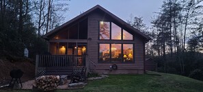Une cabane en rondins à deux étages, dotée de grandes fenêtres, d’un porche avec des chaises et d’une pelouse bien entretenue.