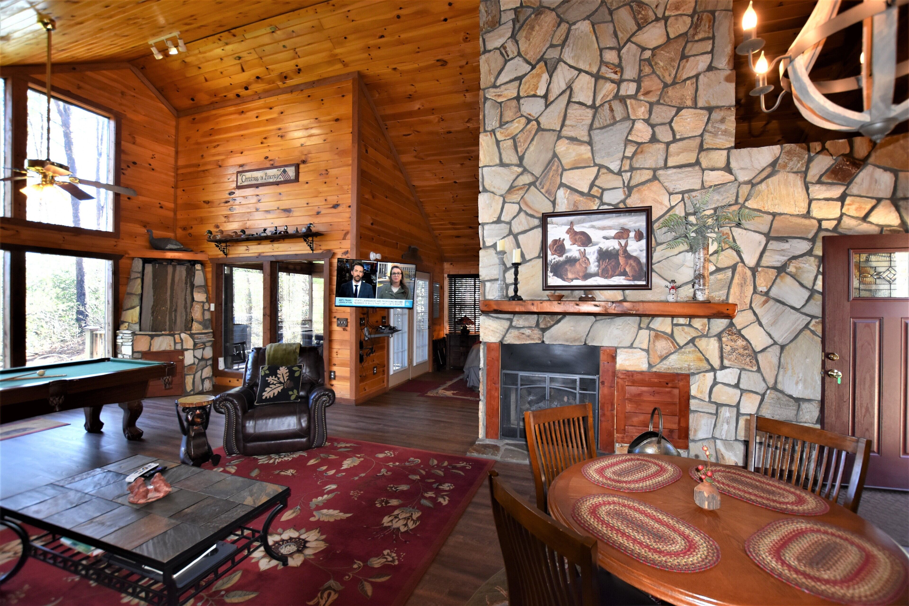 Interior acogedor de una cabaña con chimenea de piedra, techo de madera y una mesa de billar.