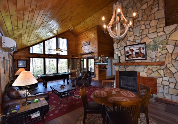 Un intérieur chaleureux de chalet avec une cheminée en pierre, un plafond en bois et une table de billard.