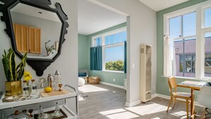 Una habitación luminosa con suelo de madera, una mesa de comedor con sillas, un espejo grande y una ventana con cortinas.