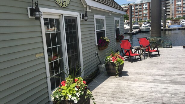 A waterfront building with a sign reading "Turtle," featuring a dock with red chairs and potted plants.