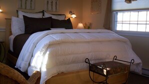 A neatly made bed with white and dark bedding, a bedside lamp, and a window with blinds.