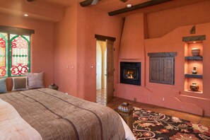 A bedroom with a large bed, a fireplace, and a stained glass window.