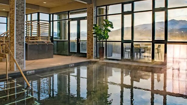 Une piscine intérieure avec des parois en verre transparent, un escalier et une grande plante.