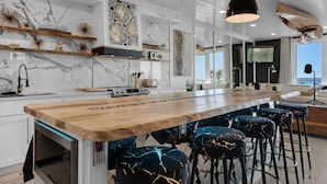 A modern kitchen with a marble backsplash, wooden bar counter, and bar stools.
