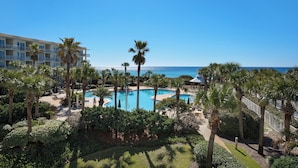 A resort with a pool surrounded by palm trees and a view of the ocean.