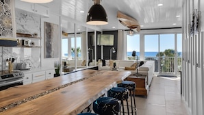 A modern kitchen with a wooden island, bar stools, and a view of the ocean.