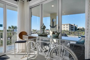 Enjoy the view from this balcony with a glass table, chair, and cushion, overlooking a residential area with palm trees.