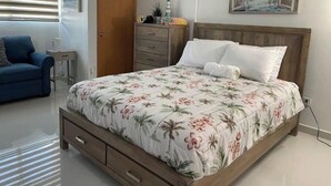 Ein Schlafzimmer mit einem Bett, einem Schminktisch, einem Nachttisch, einem blauen Sofa und einem Fenster mit Jalousien.