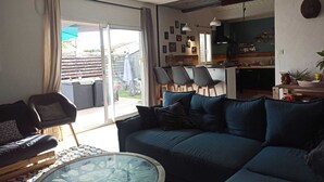 Una sala de estar con un sofá, sillas, una mesa de centro de vidrio y un ventanal corredizo que da a un patio.