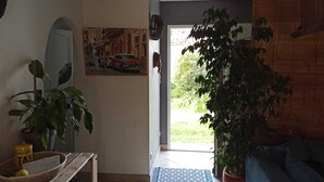 Una sala de estar con una puerta que da al exterior, un cuadro en la pared y una planta en maceta.