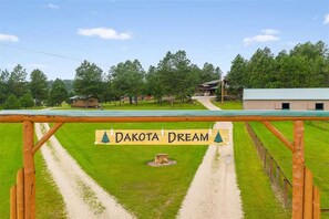 Een landelijk landschap met een bord waarop 'Dakota Dream' staat en een onverharde weg die naar een blokhut leidt.