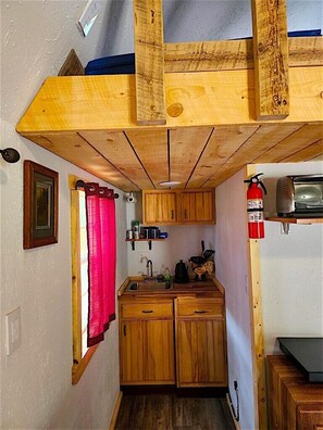 Een kleine keuken met houten kastjes, een spoelbak, een klein aanrecht en een rood gordijn.