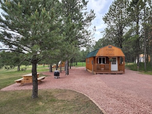 Een rustieke chalet met een veranda, omringd door pijnbomen en grindpaden.