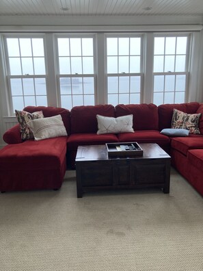 A living room with a red sectional sofa, a wooden coffee table, and large windows with a view of the water.